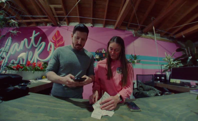 A man and woman stand together in a shop while tallying receipts