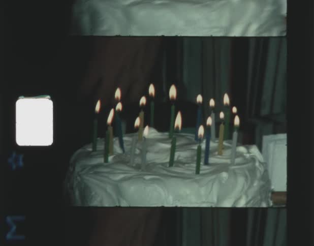 A heavily frosted cake has a ring of lit candles on top of it