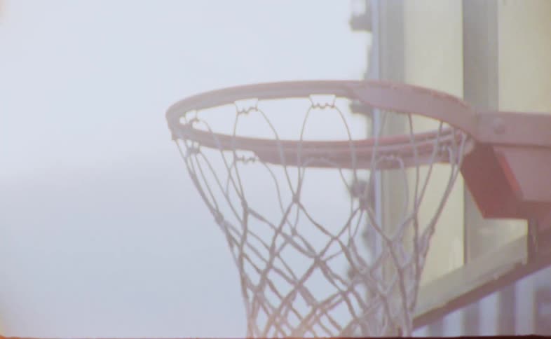 Man in park catches basketball after shot and throws it as mother pushes baby buggy in the background