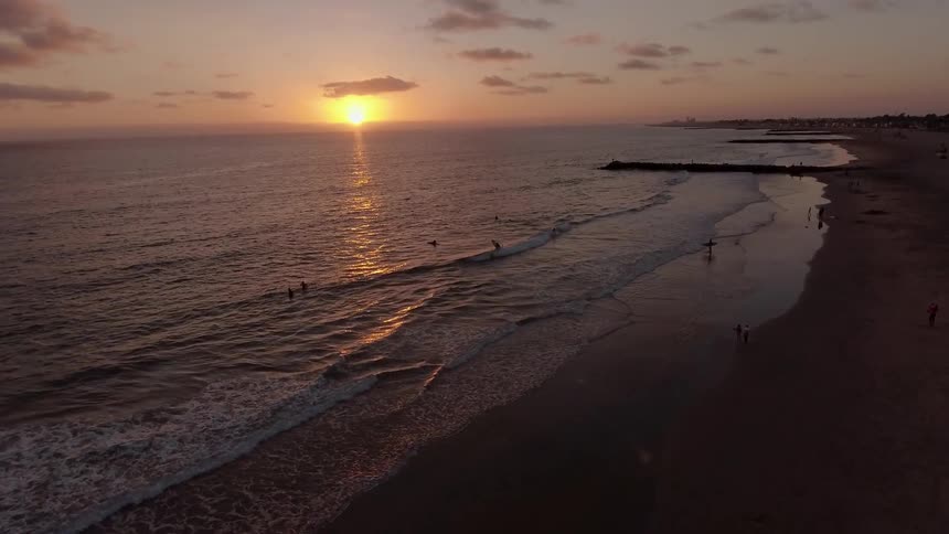 People are in the water on the beach at sunset