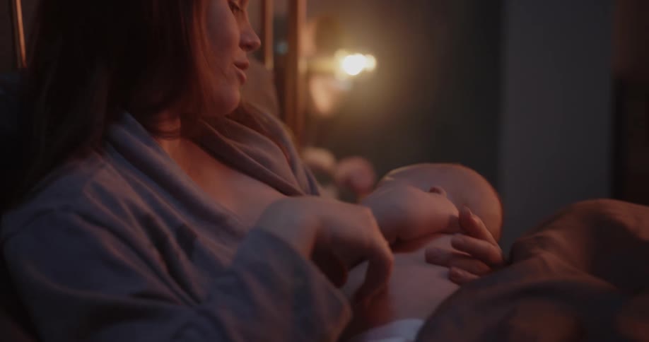 A woman is home in bed nursing her infant in the evening