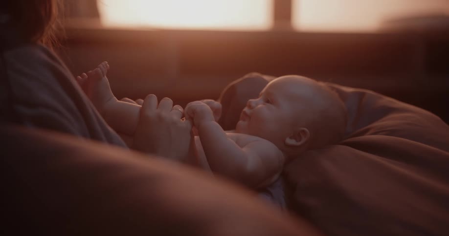 Mother with brown hair kisses newborn babys feet in bedroom