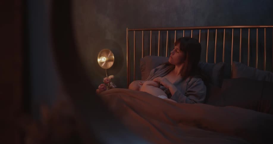Mother with brown hair breastfeeds baby son sitting on bed