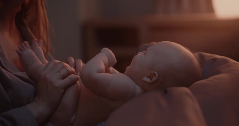 Mother smiles and laughs while kissing feet of baby in her lap