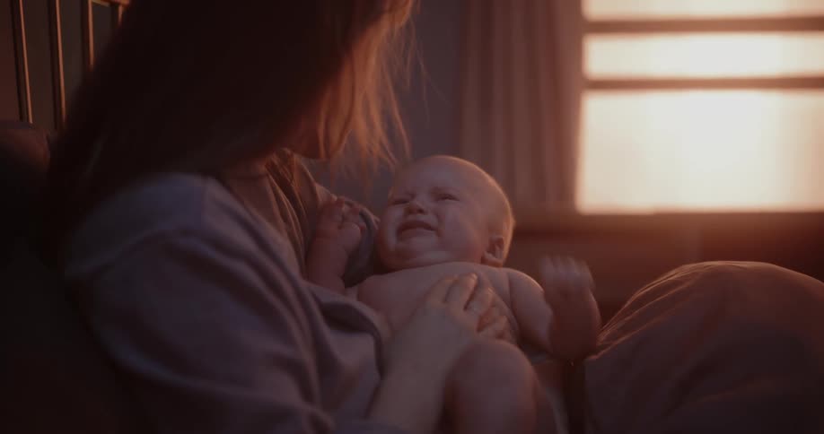 A mother rocks her baby in her lap as it cries