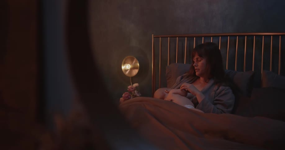 Mirror reflects woman yawning while she lies in bed nursing her baby