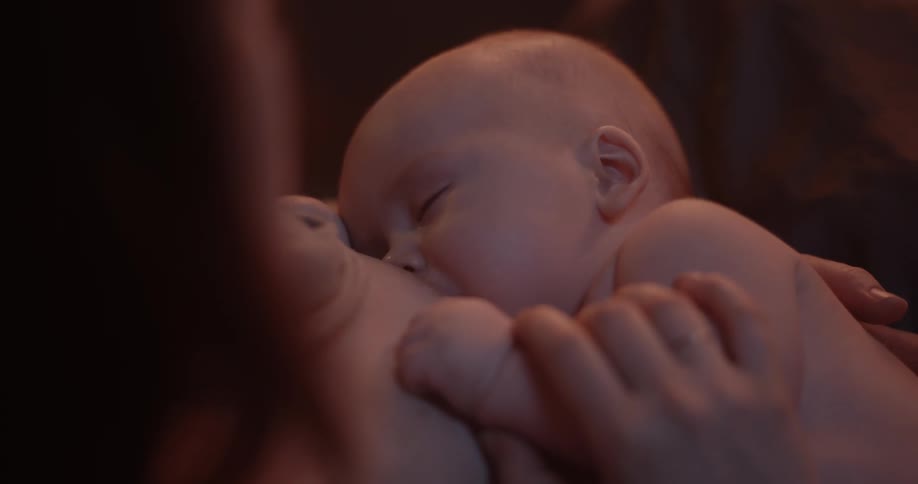 Mother breastfeeds baby son stroking his arm