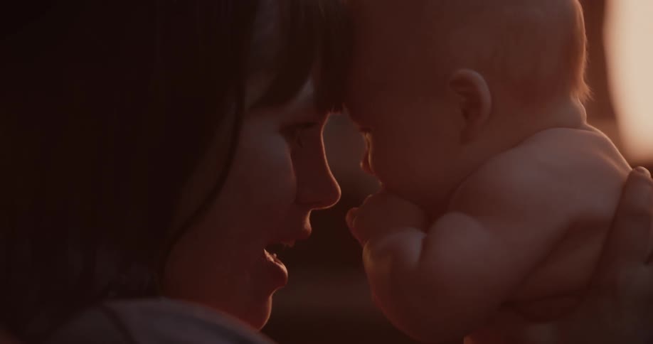 Mother with bangs holds newborn baby at sunset