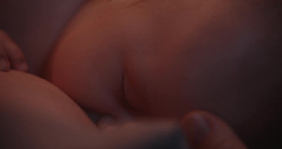 A baby is peacefully sleeping on a bed while his mother gently touches his head with an expression of love and affection