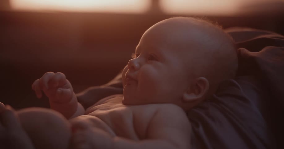 A baby is lying down moving their arms and smiling