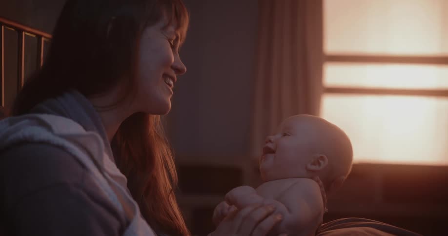 Mother and baby interacting with each other in the morning sitting on bed eye contact laughing and smiling