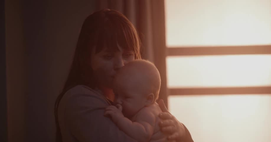 Mother with brown hair holds newborn baby in her arms in room