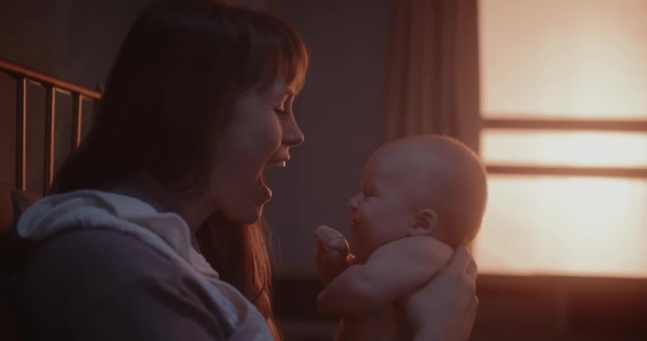 A woman holds a baby in front of her face and talks smiles while they gaze into each others eyes