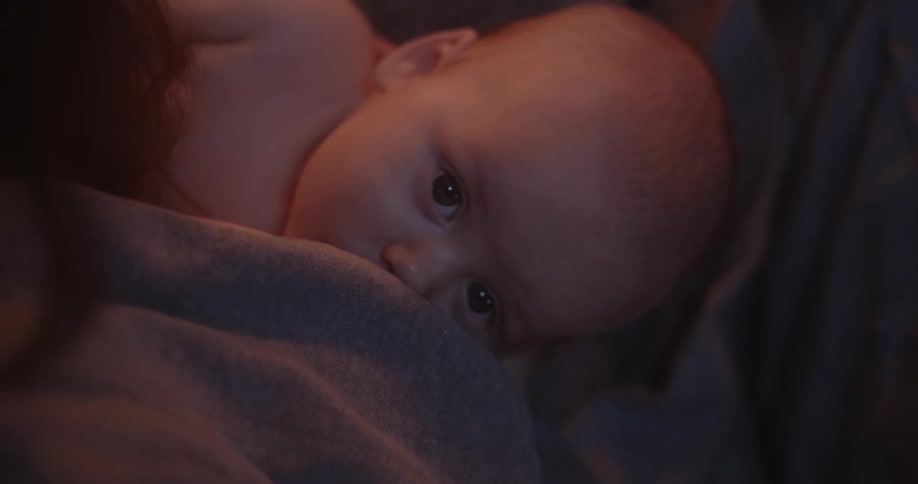 A woman is holding her baby and rubbing their head as she nurses the infant