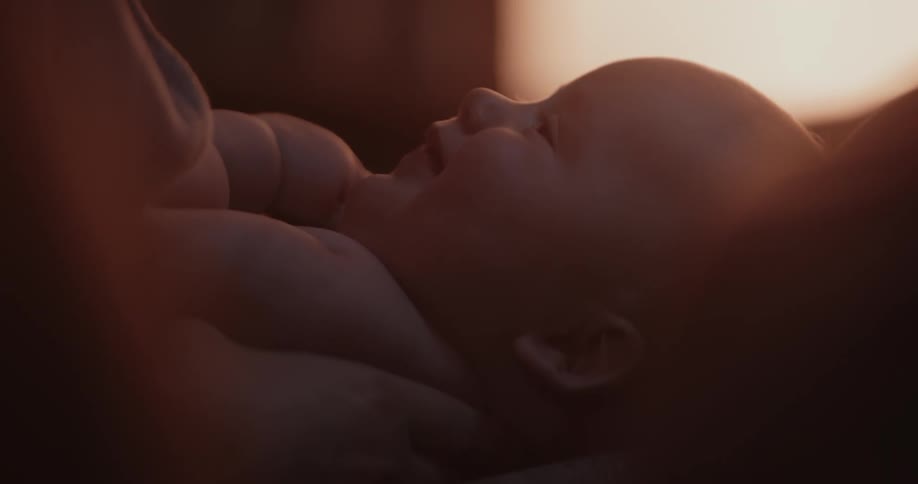 Baby looks up to its mother in dimly lit room