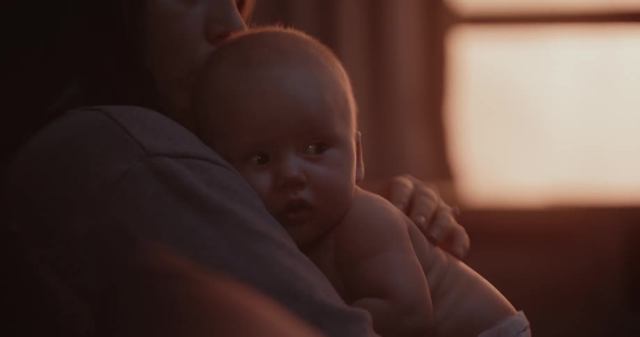 A mother helds her baby against her chest and rubs their back gently