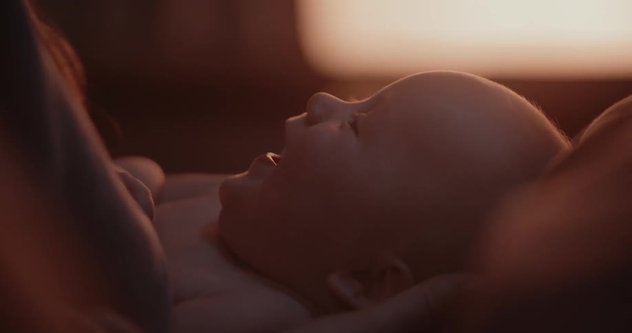 Sun shines through window into dim room where mother holds smiling baby