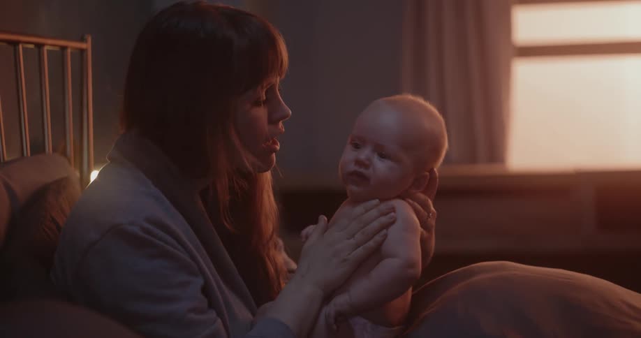 A woman is sitting up holding her baby and talking to calm them down