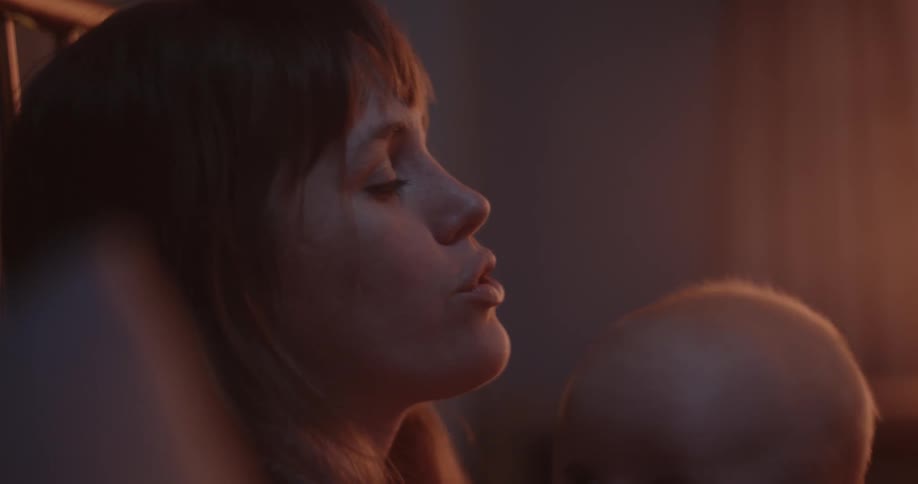 Mother with brown bangs rocks baby in her arms sitting on bed