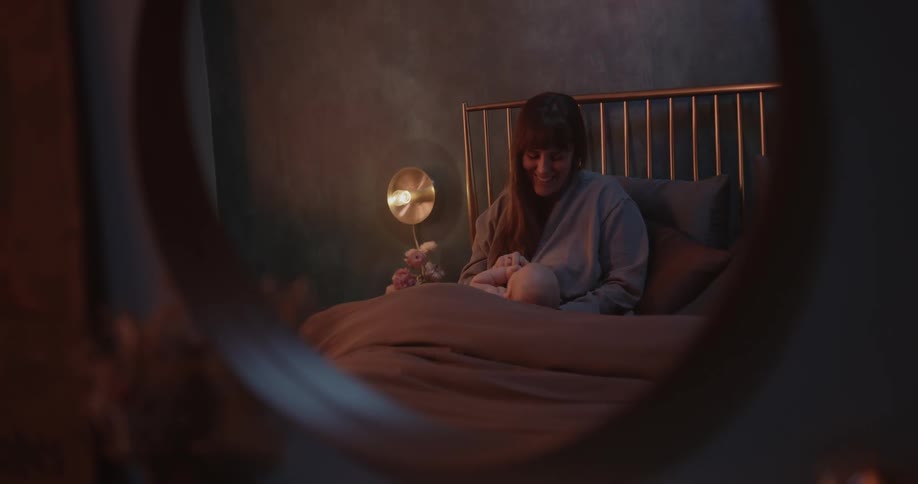 A woman is sitting up in bed playing with her baby and talking to her
