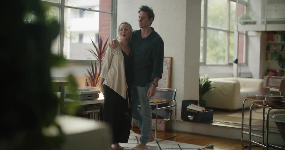 Man with dark blue shirt jeans and blonde woman with black dress and brown cardigan rearrange the living room