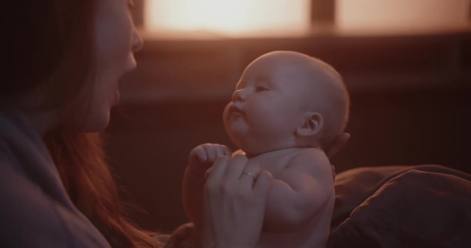 Mother with brown hair holds newborn baby with diaper laughing in room