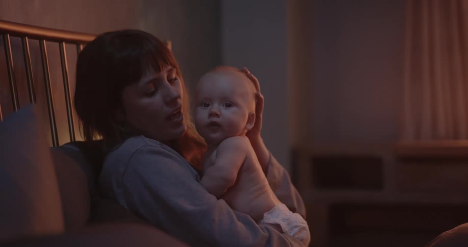Mother with brown bangs holds newborn baby in her arms in the living room