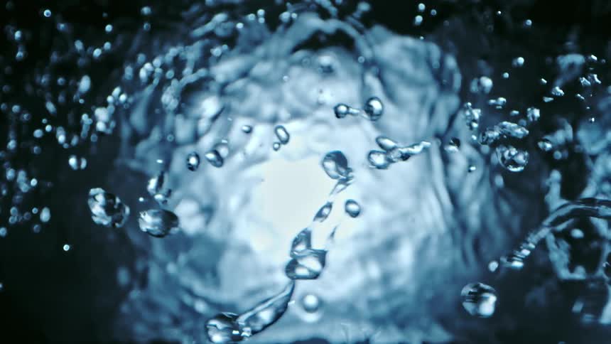 Light shines on water as it ripples and moves and droplets splash across the air above