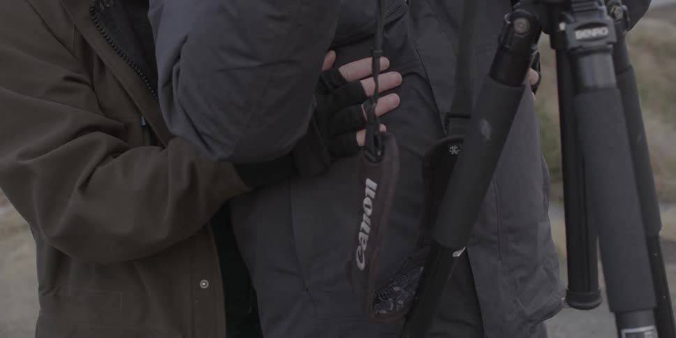 A person wraps their hands around another person with a camera