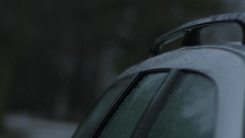 Snow falls onto frosted vehicle parked near woods