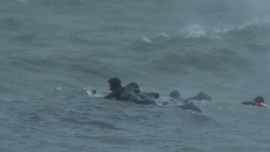 Three surfers swim side by side on their surfboards
