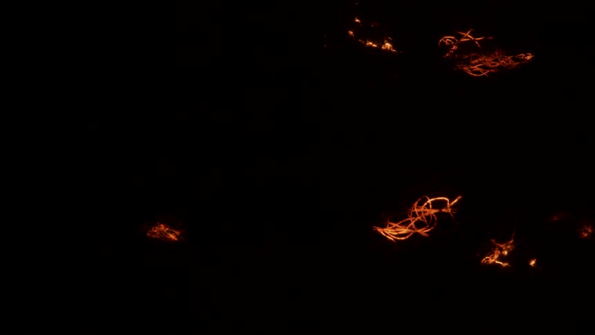 Glowing orange lights move and spread in the darkness leaving trails of illuminated light in all directions