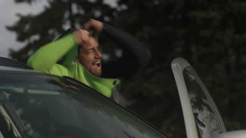 A man is putting on wetsuit swimming gear near his car