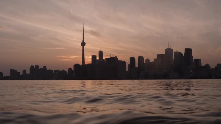 Distant buildings and high rise buildings of the Toronto skyline being silhouetted against the sunset