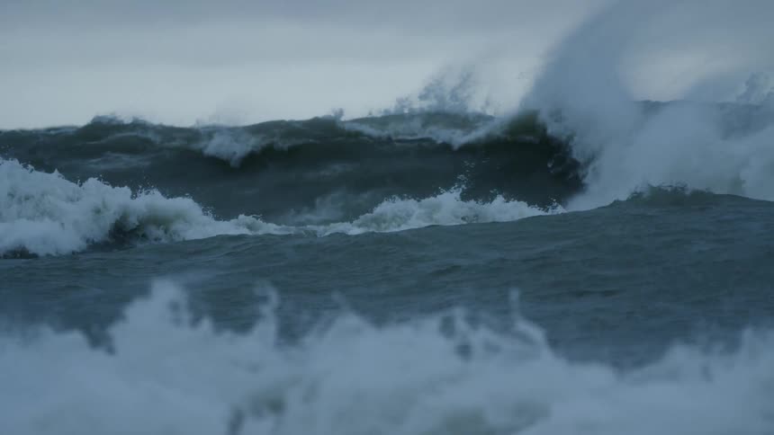 Large waves flow and generate whitewater as they collapse on ocean under an overcast sky