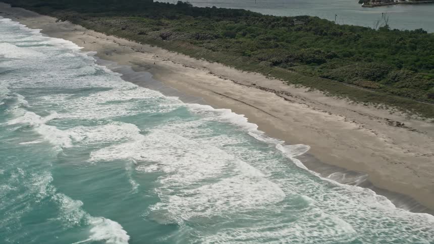 An aerial view of waves lapping an empty beach on the Florida coast in Tequesta with partly cloudy skies perfect for sightseeing and recreation