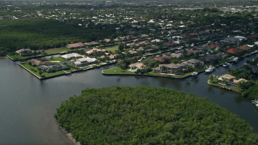 Aerial footage of approaching waterfront homes in Hobe Sound Florida after flying over Indian River and showcasing the lush greenery and picturesque waterways of the area