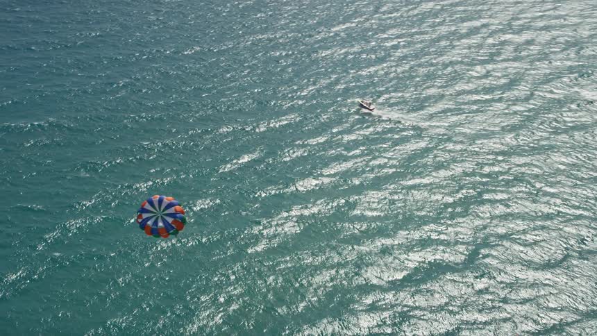 Aerial footage of a parasailer gliding above the clear blue waters of Riviera Beach Florida