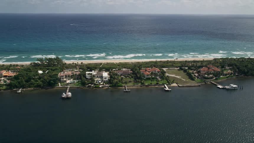 An aerial video shows a row of luxurious mansions with docks along the lakeside in Manalapan Florida
