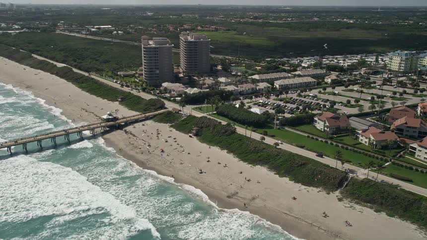 Approaching Juno Beach fishing pier capturing a beautiful sunny day with beachgoers and residences in the surrounding area