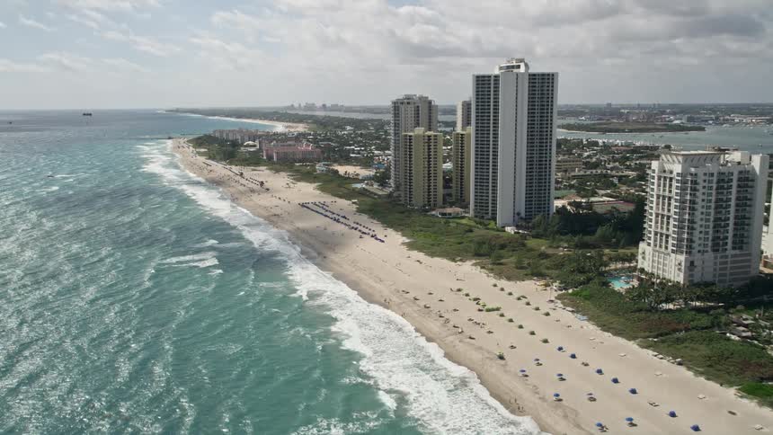 An aerial view of beautiful condominium complexes by the beach in Riviera Beach Florida showing shoreline residential buildings and a motorboat pulling a parasail