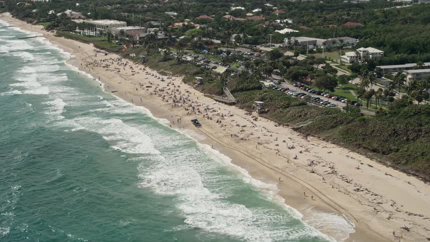 Approaching Boynton Beach Florida by air this sunny clip features sunbathers relaxing on the shoreline while waves crash against the sand