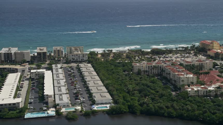 Aerial flyover of Palm Beach Floridas waterfront hotels and apartment buildings showcasing the surrounding shoreline water bodies and residential neighborhoods