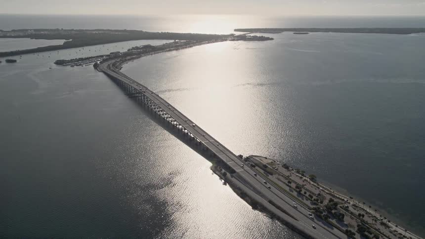 Aerial footage of the Rickenbacker Causeway in Florida with light traffic and a side view of cars driving over Biscayne Bay