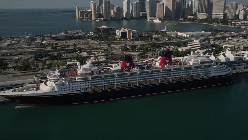 A Disney Cruise Ship is seen orbiting through the clear blue skies of Miamis port surrounded by vessels and shoreline