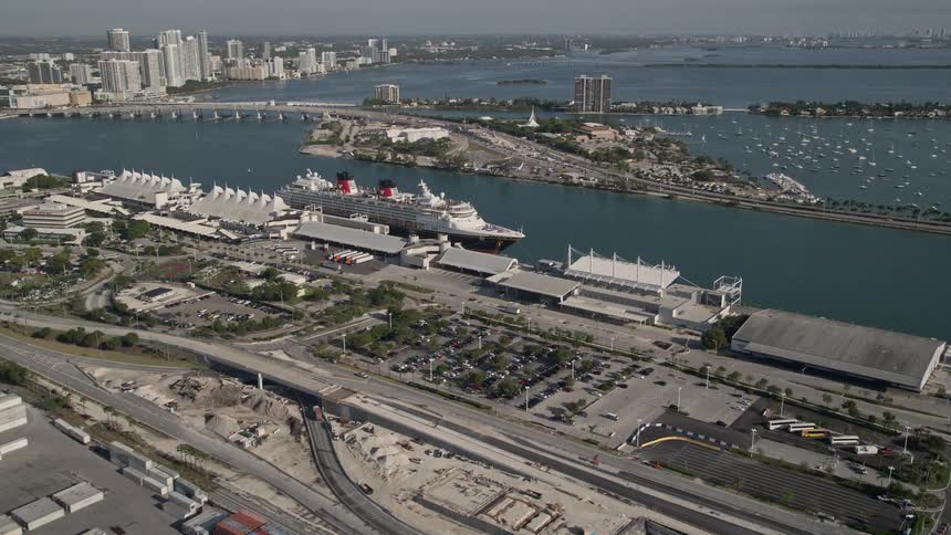 Approaching and flying by a Disney cruise ship docked at Port of Miami providing a stunning aerial view of the luxury liner against the backdrop of skyscrapers and Biscayne Bay on a sunny day in Southern Florida