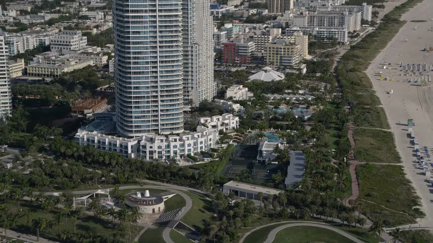 An aerial footage of South Pointe Park in South Beach Miami Beach Florida showcasing the shoreline high-rise buildings and beachgoers enjoying the sunny day