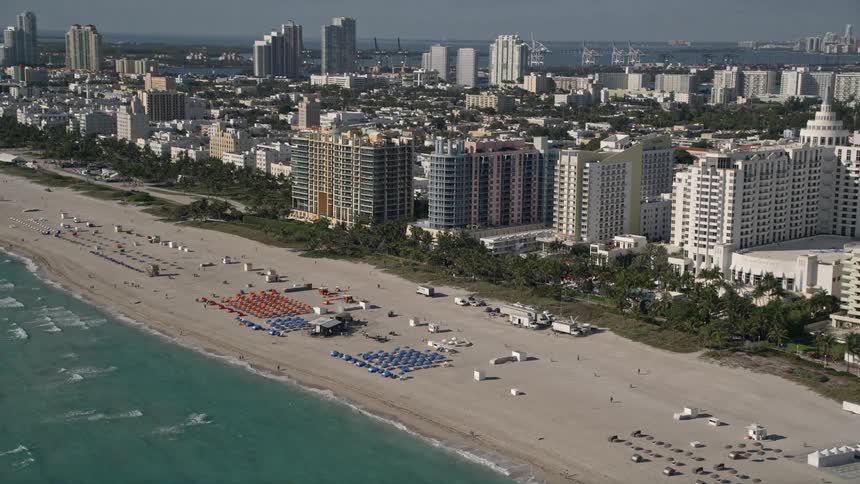 A stunning aerial view of South Beach in Miami Florida as the camera pans over the coastline with its luxurious hotels and bustling beach-goers enjoying the sunshine and recreation