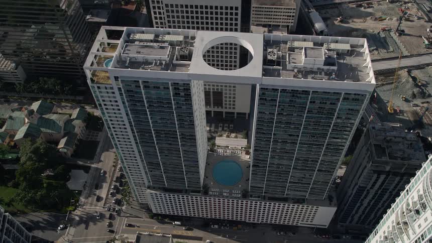 Approaching 500 Brickell West Tower the aerial footage tilts to a birds eye view of the modern high rise and tall buildings overseeing the busy streets of downtown Miami Florida
