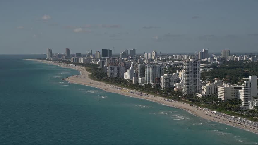 Flying over South Beach and Miami Beach this 5K aerial footage captures hotels apartments and a busy coastal beach with people enjoying the sunshine and recreation activities